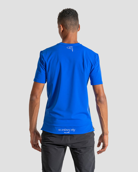 GoofyPRO Cayton Core Performance Tshirt in racing blue with short sleeves, rear. White embroidered 'no ordinary way' in white on waistband. White embroidered logo at top of neck. Worn by male model.