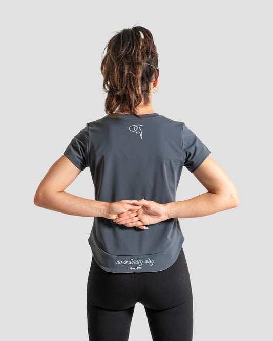 GoofyPRO Cayton Core Performance Tshirt in titanium with short sleeves, rear. White embroidered 'no ordinary way' in white on waistband. White embroidered logo at top of neck. worn by female model