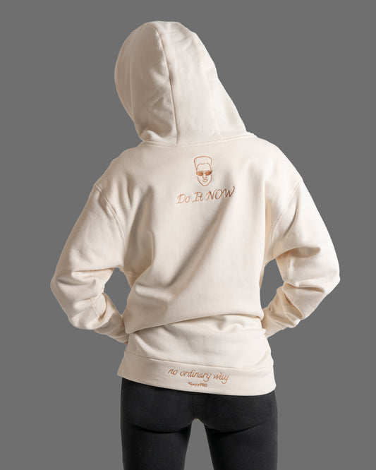 GoofyPRO Daymer fleece hoodie in cream with Rose Gold embroidery of a face and the words Do It NOW on on top of neck and Rose Gold and embroidery on waistband 'no ordinary way'.  Worn by female model